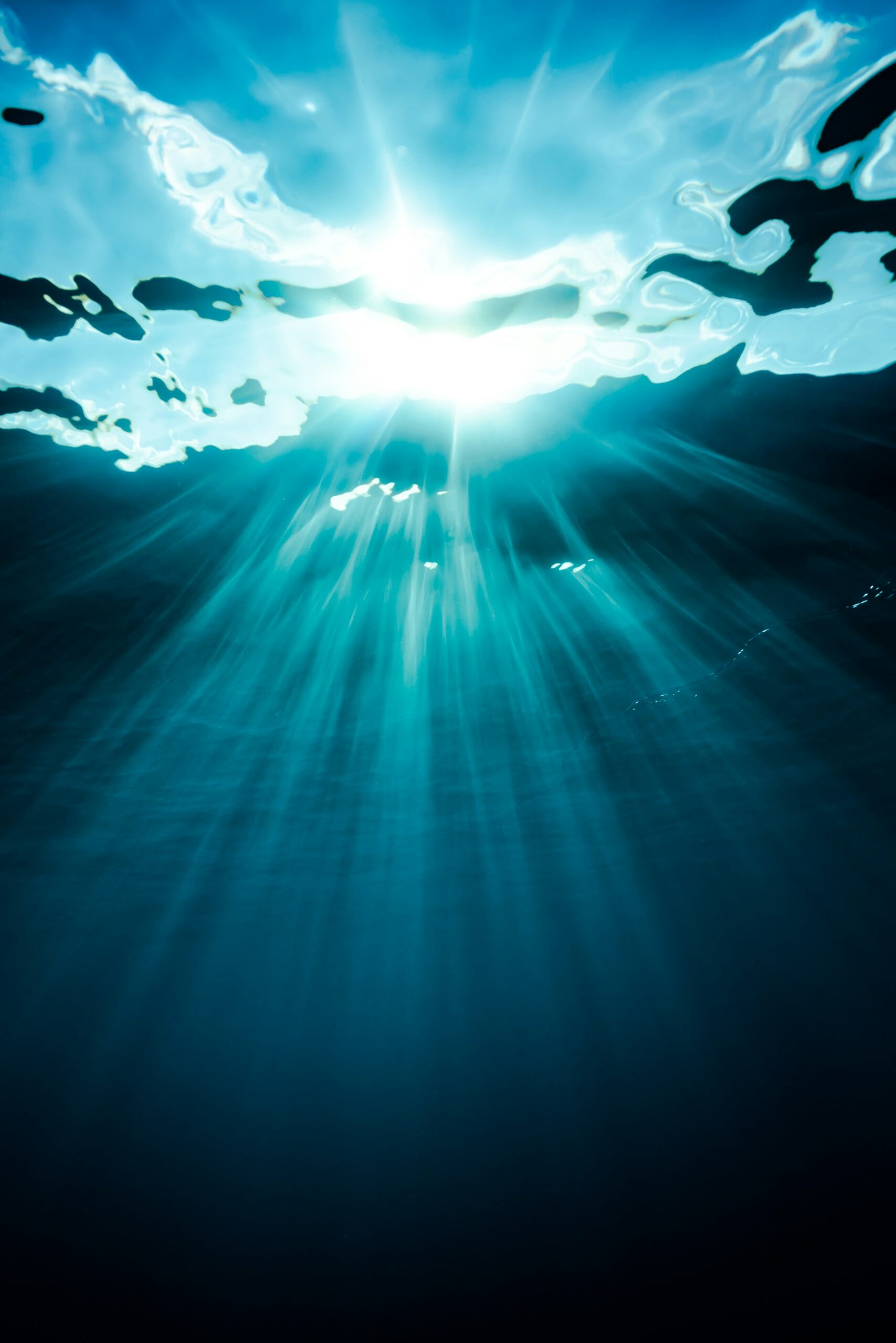 Helle Sonnenstrahlen, die durch die Wasseroberfläche in die blaue Tiefe scheinen.